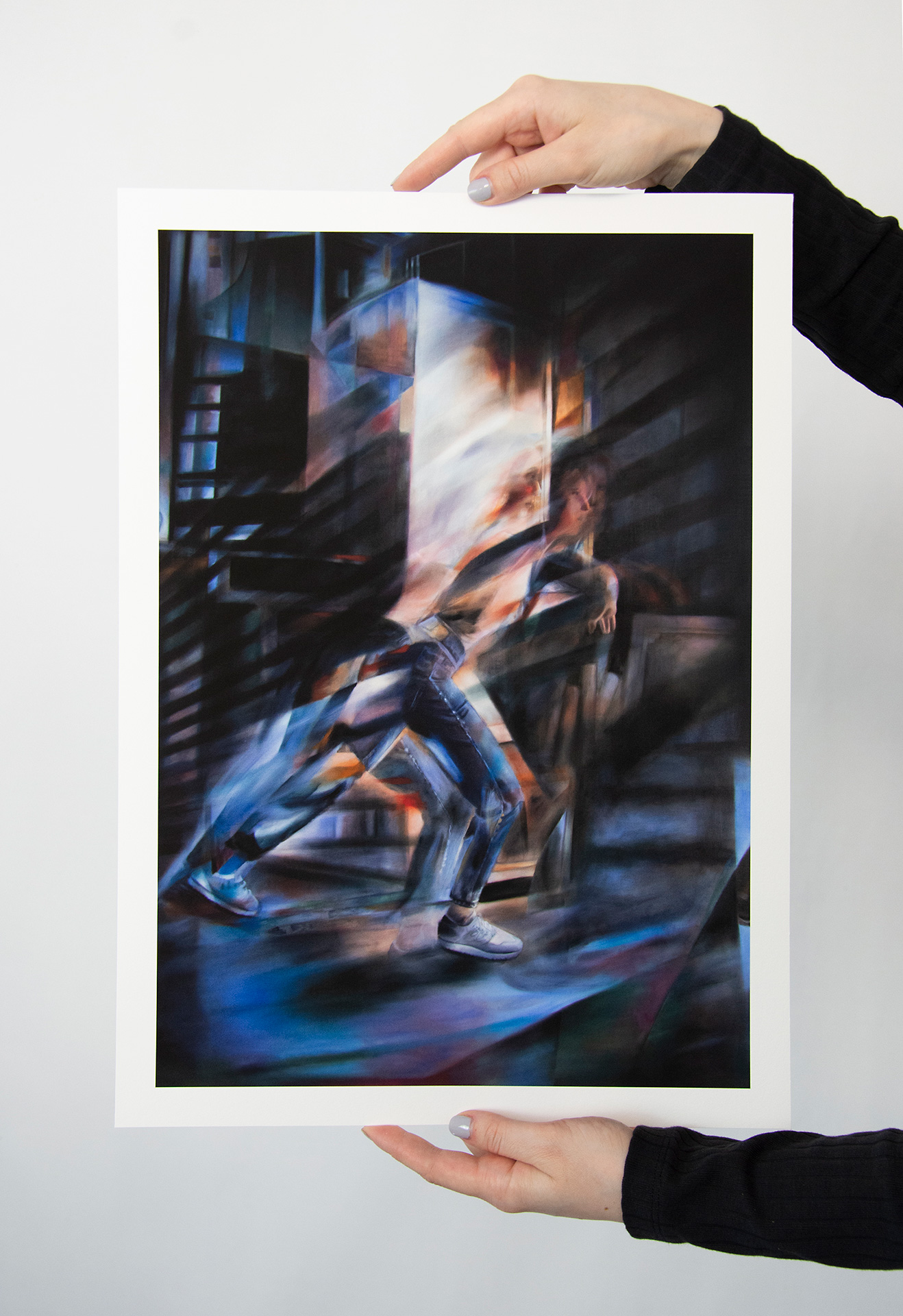 "Vortex 1" fine art print by Evelina Klanikova held in hand in front of a white wall, depicting an abstract representation of a running person with motion blur effects in shades of blue and green.